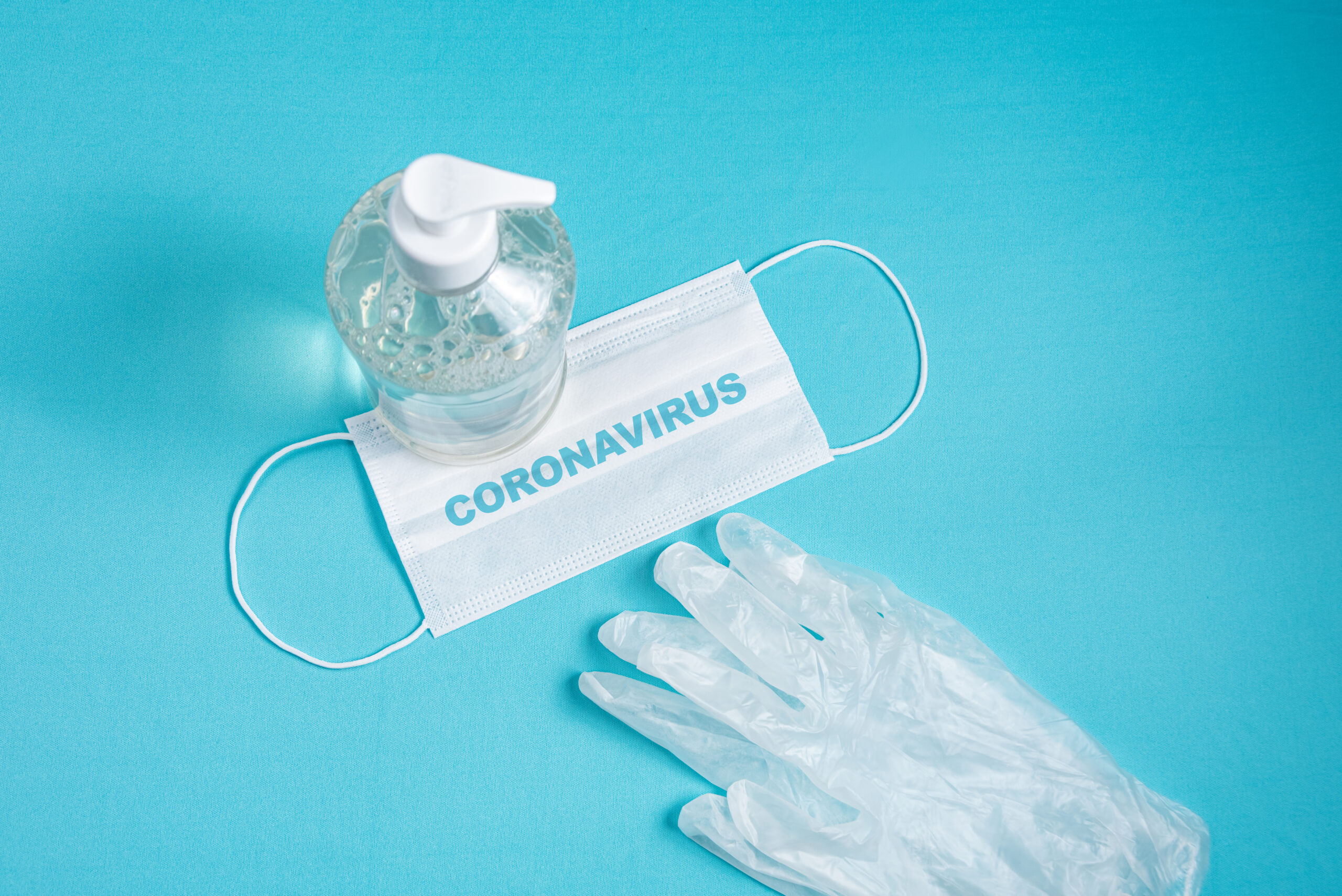 Container with alcohol gel, gloves and surgical mask on the ligh